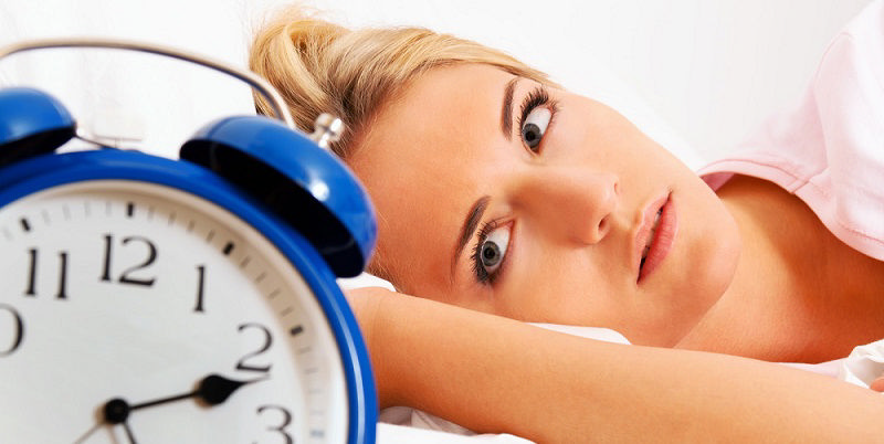 دختری که به دلیل اختلال خواب بی‌خواب شده و به ساعت خیره شده است