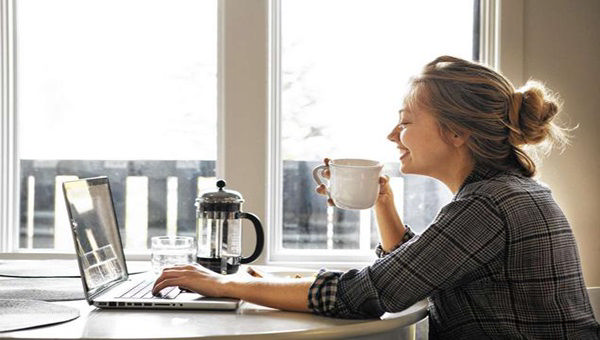 دختری که صبح زود در حال خوردن قهوه و کار با لپ تاپش است