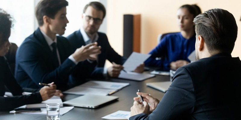 چند مرد و یک زن در حال مذاکره دور یک میز با لباس‌های رسمی نشسته‌اند