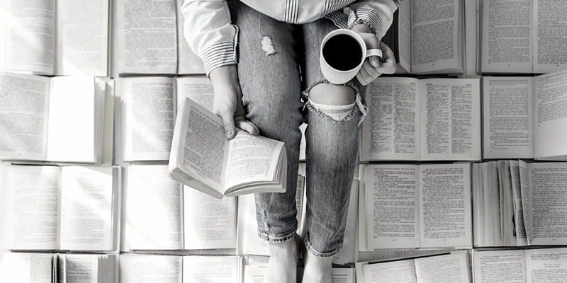 دختری که با یک لیوان قهوه بر روی چندین کتاب باز نشسته است