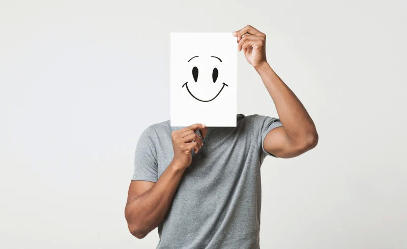 مردی که کاغذ آچهار با صورتکی خندان را جلوی صورتش گرفته است