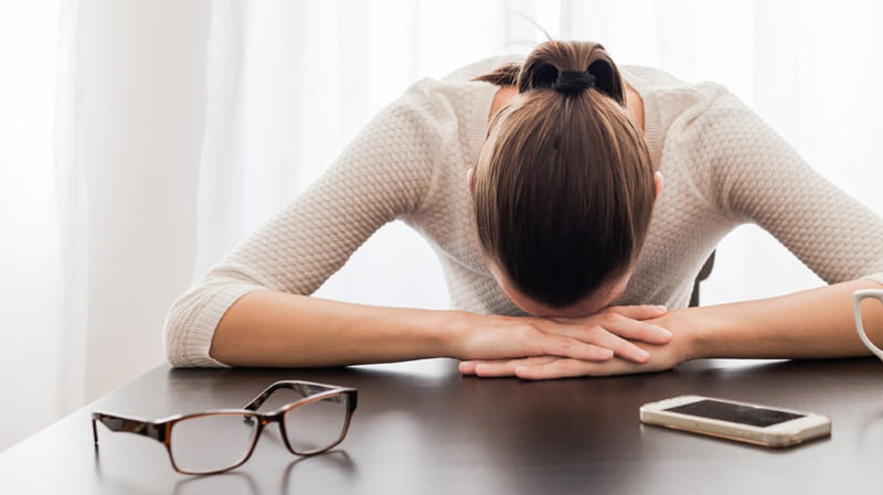 راههای غلبه بر کمالگرایی، زنی که از شدت کلافگی سرش را روی میز گذاشته است